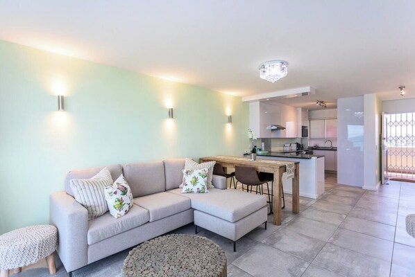 A modern living room with a sectional sofa, a dining table, and a kitchen in the background.