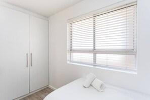 A bedroom with a bed, a wardrobe, and a window with blinds.