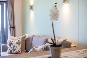 Un salon moderne avec un canapé, des coussins décoratifs, une plante en pot et des lampes fixées au mur.