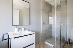 Un bagno moderno con lavandino bianco, uno specchio grande e cabina doccia in vetro.