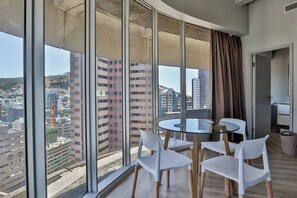 A modern hotel room with large windows, a round glass table, and white chairs.