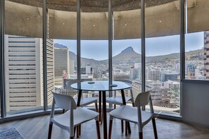 A modern interior with a round glass table and four chairs, large windows offering a cityscape view.
