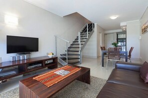 Un salon moderne doté d’un téléviseur à écran plat, d’une table basse en bois, d’un canapé et d’un escalier menant à un espace repas.