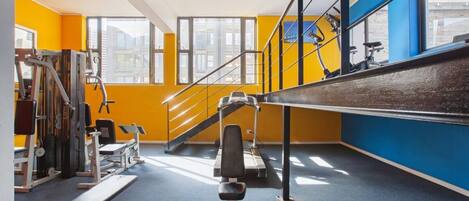 Un gimnasio con equipo de ejercicio, una escalera y ventanas amplias.