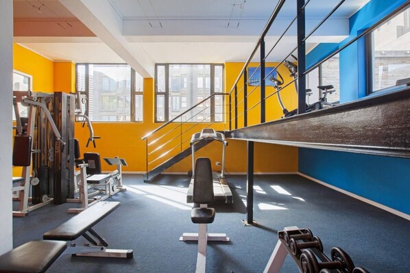 Une salle de sport équipée de matériel d’exercice, avec un escalier et de grandes fenêtres.