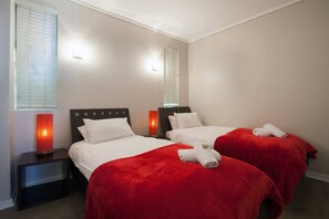 Une chambre d’hôtel avec deux lits, chacun recouvert d’une couverture rouge et agrémenté d  ’oreillers blancs, et une table de chevet avec une lampe placée entre les deux lits.