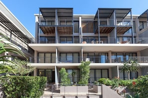 A multi-story residential building with balconies, a covered outdoor area, and greenery.