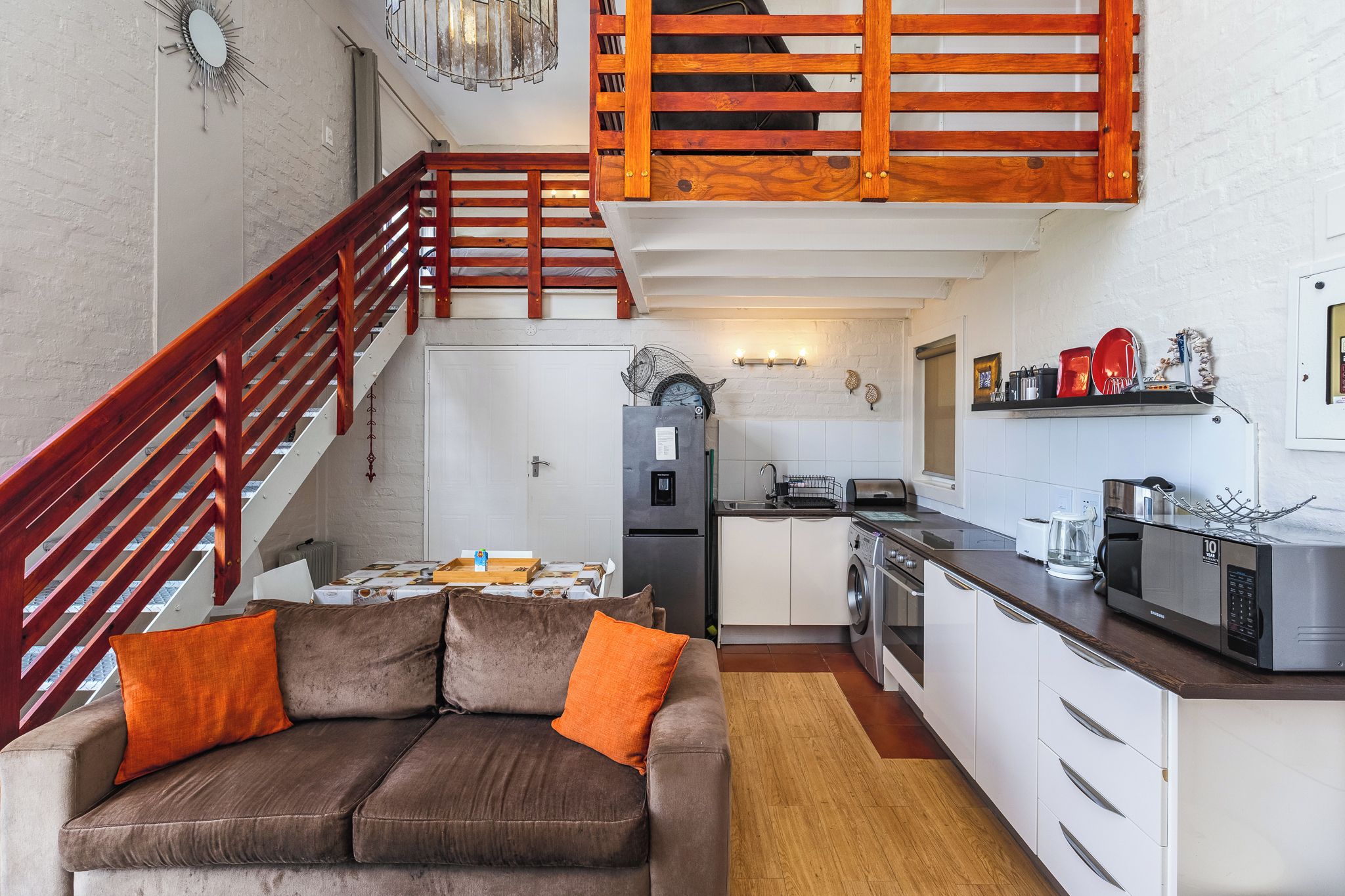 A compact living space with a sofa, kitchenette, and a staircase.