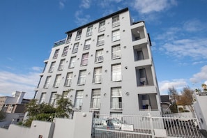 Un edificio residenziale a più piani con balconi, un ingresso carrabile e cielo sereno.