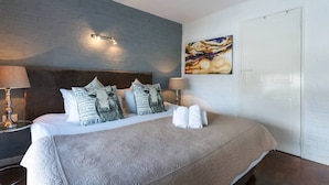 A hotel room with a bed, pillows, a painting, and a nightstand. - Harbour Terrace 48 by Ctha (Cape Town)