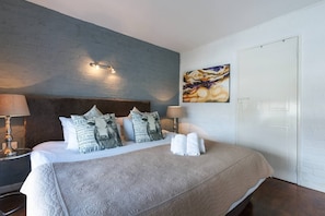 Una camera d'albergo con un letto, cuscini, un quadro e un comodino.