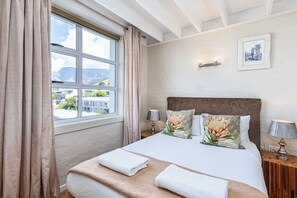 A hotel room with a large bed, two bedside lamps, a window with curtains, and a framed picture on the wall.