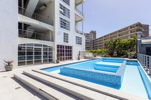 A modern building with a rooftop pool area, featuring a clear blue pool with steps leading into it.