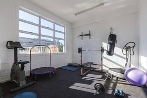 Une salle de sport équipée d’un tapis de course, d’un banc de développé couché, d’un sac de frappe et de poids libres.