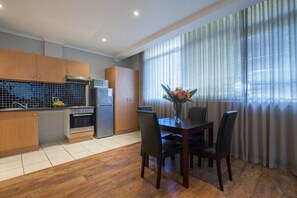 Une cuisine moderne avec des meubles en bois, un four encastré et un réfrigérateur. On y trouve une table à manger avec des chaises et un vase de fleurs.