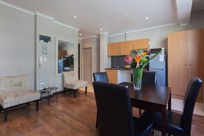 A modern living room with a dining table, two sofas, and a kitchen in the background.