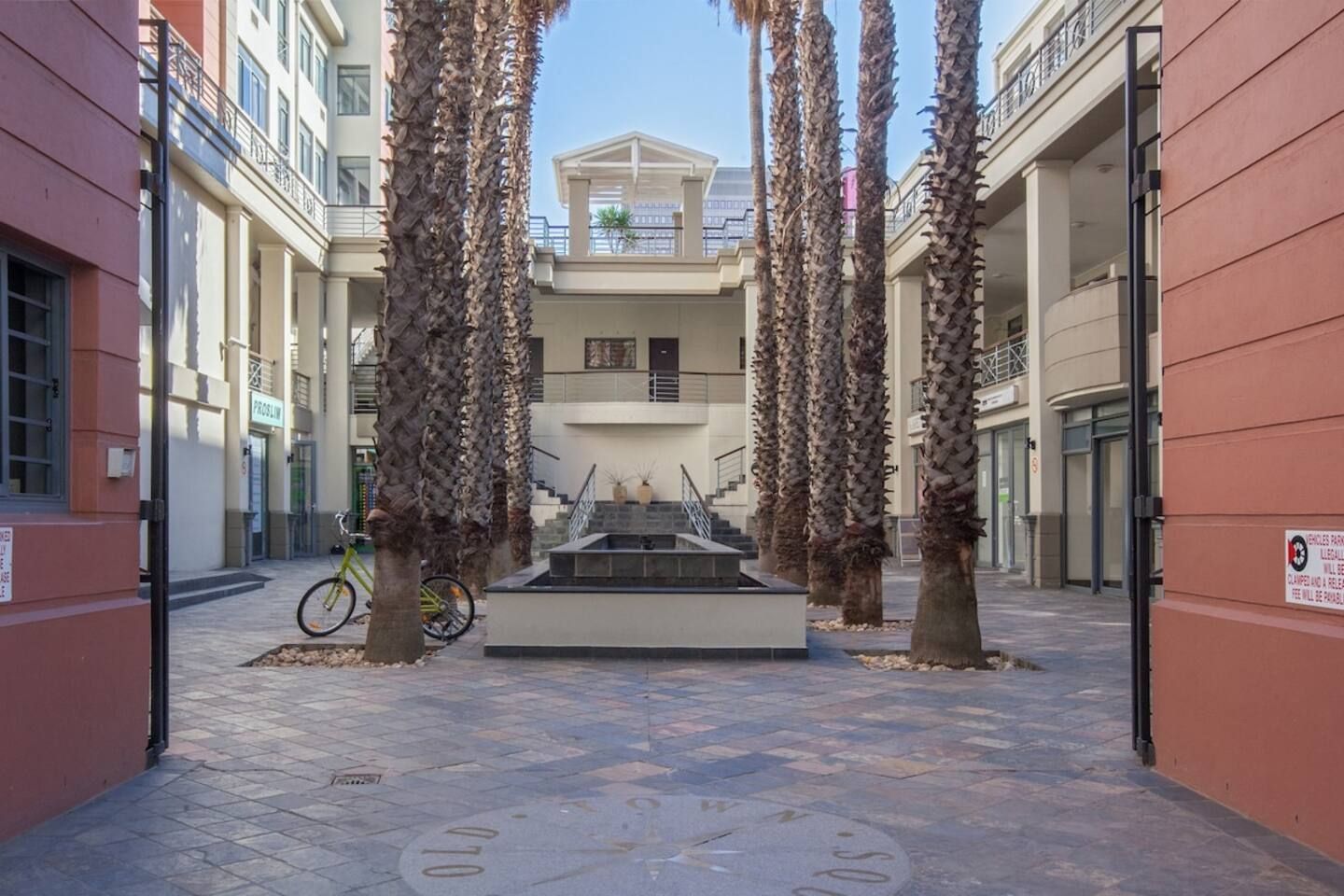 Een binnenplaats met palmbomen, een fiets en een trap naar de ingang van een gebouw.
