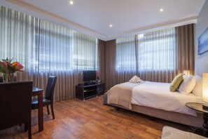 A hotel room with a bed, a desk with a chair, a TV, and curtains.