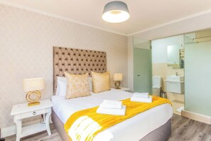 A hotel room with a large bed, a bedside table, a nightstand, a mirror, and a bathroom with a sink and toilet.