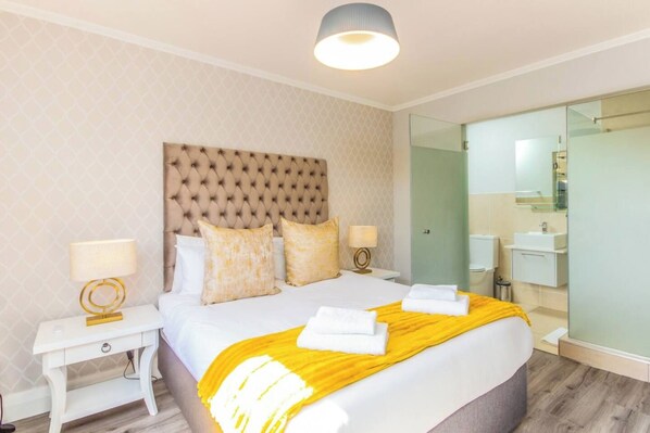 A hotel room with a large bed, a bedside table, a nightstand, a mirror, and a bathroom with a sink and toilet.