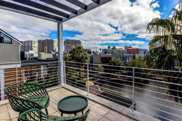 A balcony with a view of a cityscape, featuring a metal railing and a small table with chairs.