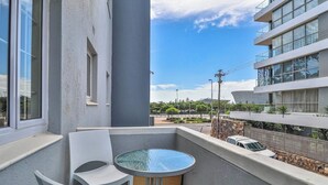 A balcony with a glass table and two white chairs, overlooking a street with modern buildings and a clear sky. - Eaton Square 2 by Ctha (Cape Town)