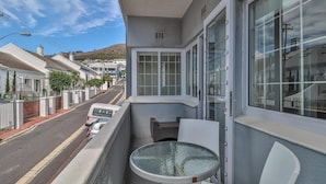 A balcony with a glass table and chairs, overlooking a street with parked cars and houses. - Eaton Square 2 by CTHA (Cape Town)