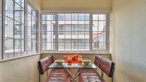 A dining area with a glass table and leather chairs, a red tray with food and drinks, and a view of buildings through large windows. - Eaton Square 2 by CTHA (Cape Town)