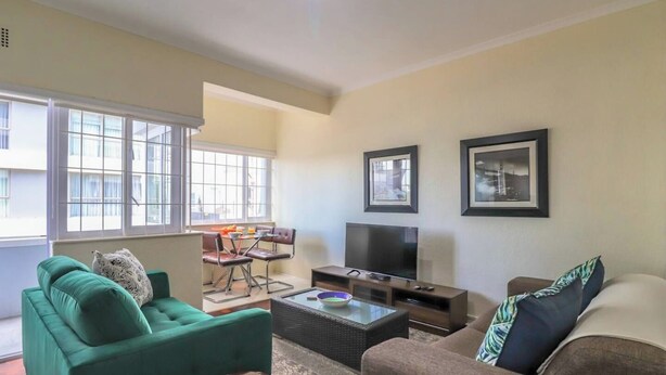 A living room with a sofa, a coffee table, a TV, and framed pictures on the wall. - Eaton Square 2 by Ctha (Cape Town)