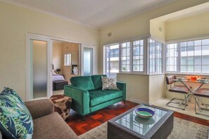 A living room with a green sofa, a glass coffee table, and a dining area with a table and chairs.