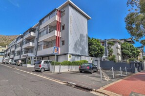 Un edificio residenziale a più piani con balconi, un'area di parcheggio e un ingresso carrabile.