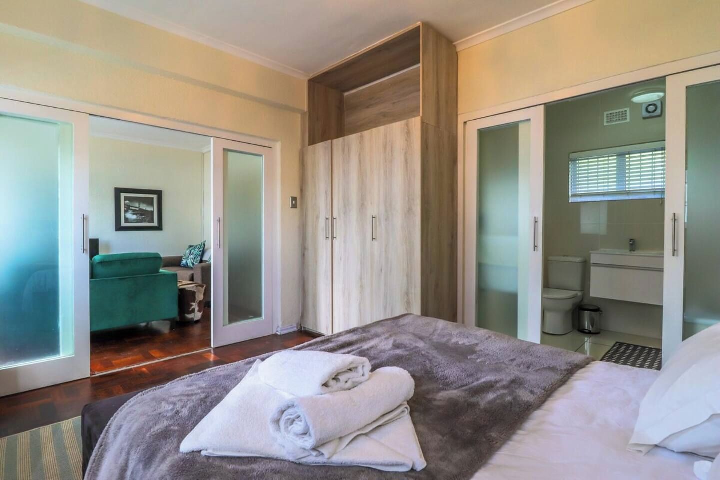 A bedroom with a bed, a wardrobe, a bathroom, and a seating area with a sofa and a chair.