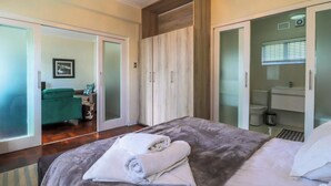 A bedroom with a bed, a wardrobe, a bathroom, and a seating area with a sofa and a chair. - Eaton Square 2 by Ctha (Cape Town)