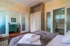 Una camera da letto con un letto, un armadio, un bagno e un angolo salotto con un divano e una poltrona.