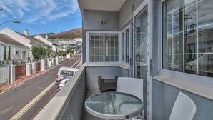 A balcony with a table and chairs, overlooking a street with parked cars and houses. - Eaton Square 2 by Ctha (Cape Town)