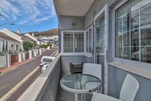 Un balcone con tavolo e sedie, affaccia su una strada con auto parcheggiate e case.