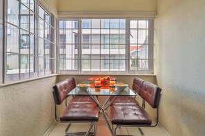 A dining area with a glass table and leather chairs, a red plate with food, and a window with a view of buildings.