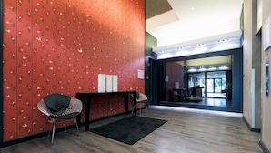 Een moderne lobby met een murenpaneel in rood patroon, een zwart tapijt en een metalen stoel.