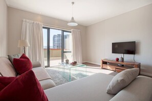 A modern hotel room with a large bed, a TV, a glass coffee table, and a balcony with curtains.