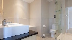 Un baño moderno con un lavamanos grande de color blanco, cabina de ducha con mampara de vidrio y un inodoro.