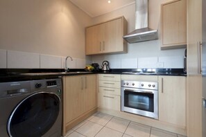 A modern kitchen with a stainless steel washing machine, a built-in oven, and wooden cabinets.
