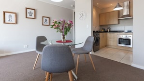 Een moderne keuken met roestvrijstalen apparatuur, een eethoek met een glazen tafel en grijze stoelen, en een wandklok.