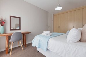 A bedroom with a bed, a desk, a chair, a wardrobe, and a hanging light fixture.