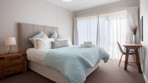 Un dormitorio con cama, mesita de noche, lámpara y escritorio con silla.