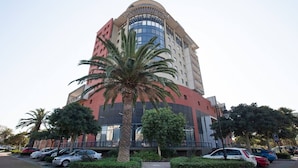 Un edificio de varios pisos con fachada curva, rodeado de coches aparcados y palmeras.