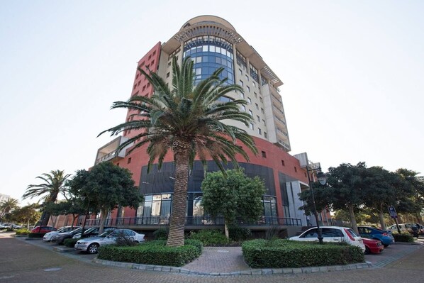A multi-story building with a curved facade, surrounded by parked cars and palm trees.