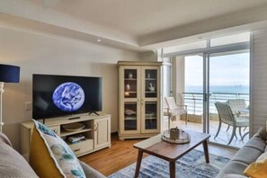 Un soggiorno con televisione, un mobile contenitore, un divano, un tavolo e un balcone con vista mare.