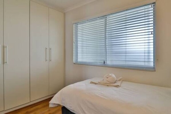 A bedroom with a bed, a window with blinds, and a wardrobe.