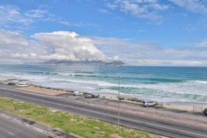 A coastal road with vehicles parked along the side, leading to the beach.