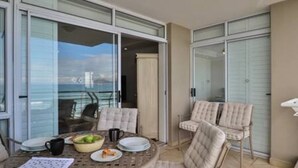 A balcony with a table set for two, chairs, and a view of the sea. - Ocean View C403 by Ctha (Cape Town)